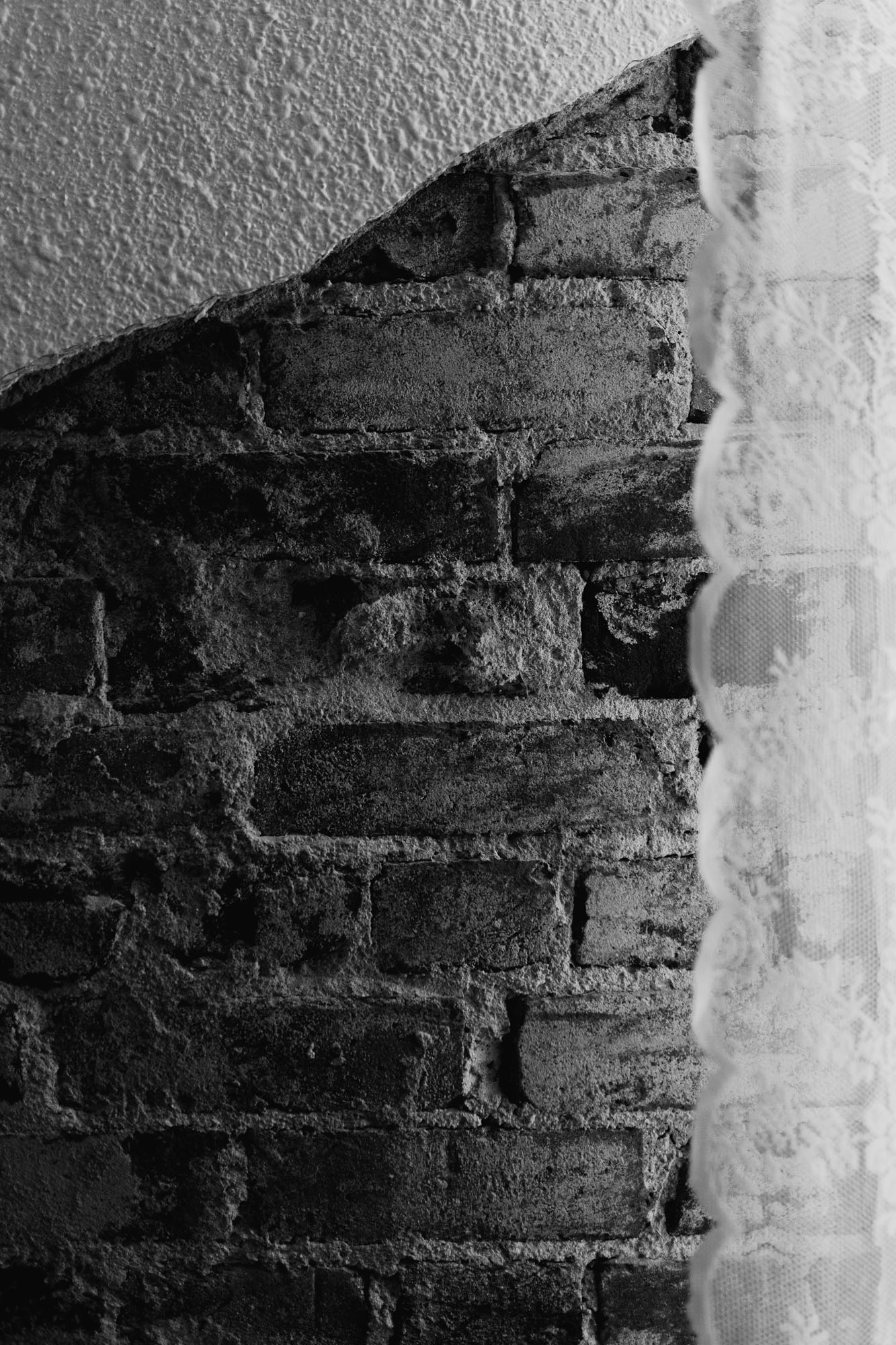 Black and white lace curtains on brick wall